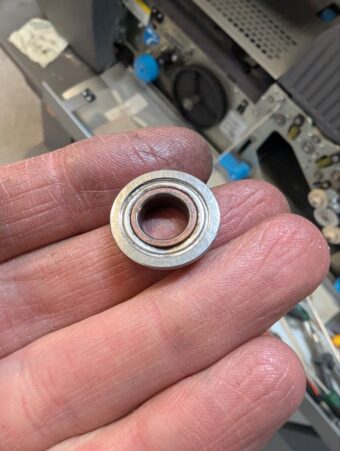 Ein defektes, durch Reibung rötlich verfärbtes Kugellager einer Kuvertiermaschine, das zum Verschleiß der mechanischen Achse geführt hat.